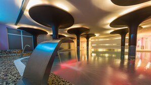 A modern hotel lobby with a large, open space, a central water feature, and a patterned floor. - Hotel Palacio Albacete & SPA (Albacete)
