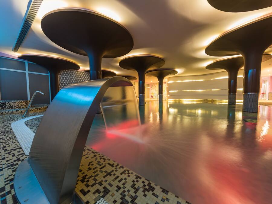 A modern hotel lobby with a large, open space, a central water feature, and a patterned floor.