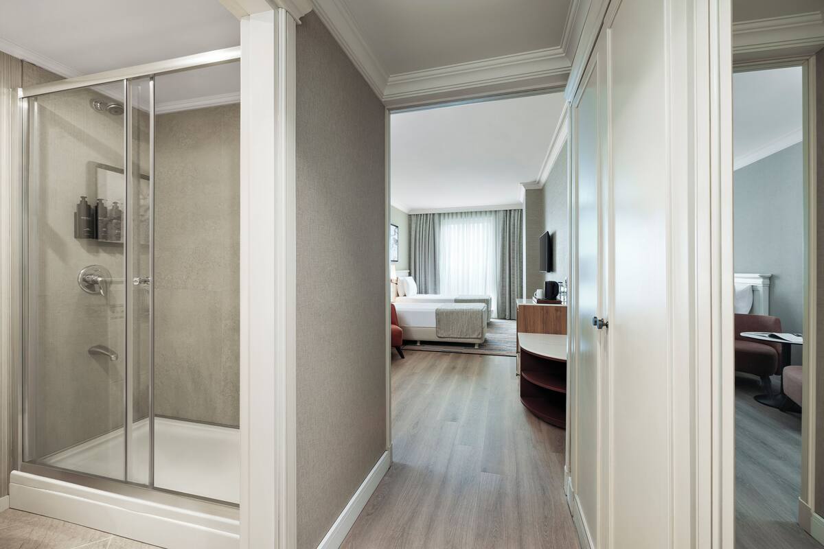 A hotel room with a glass-enclosed shower, a bed with a bedside table, a desk, and a chair.
