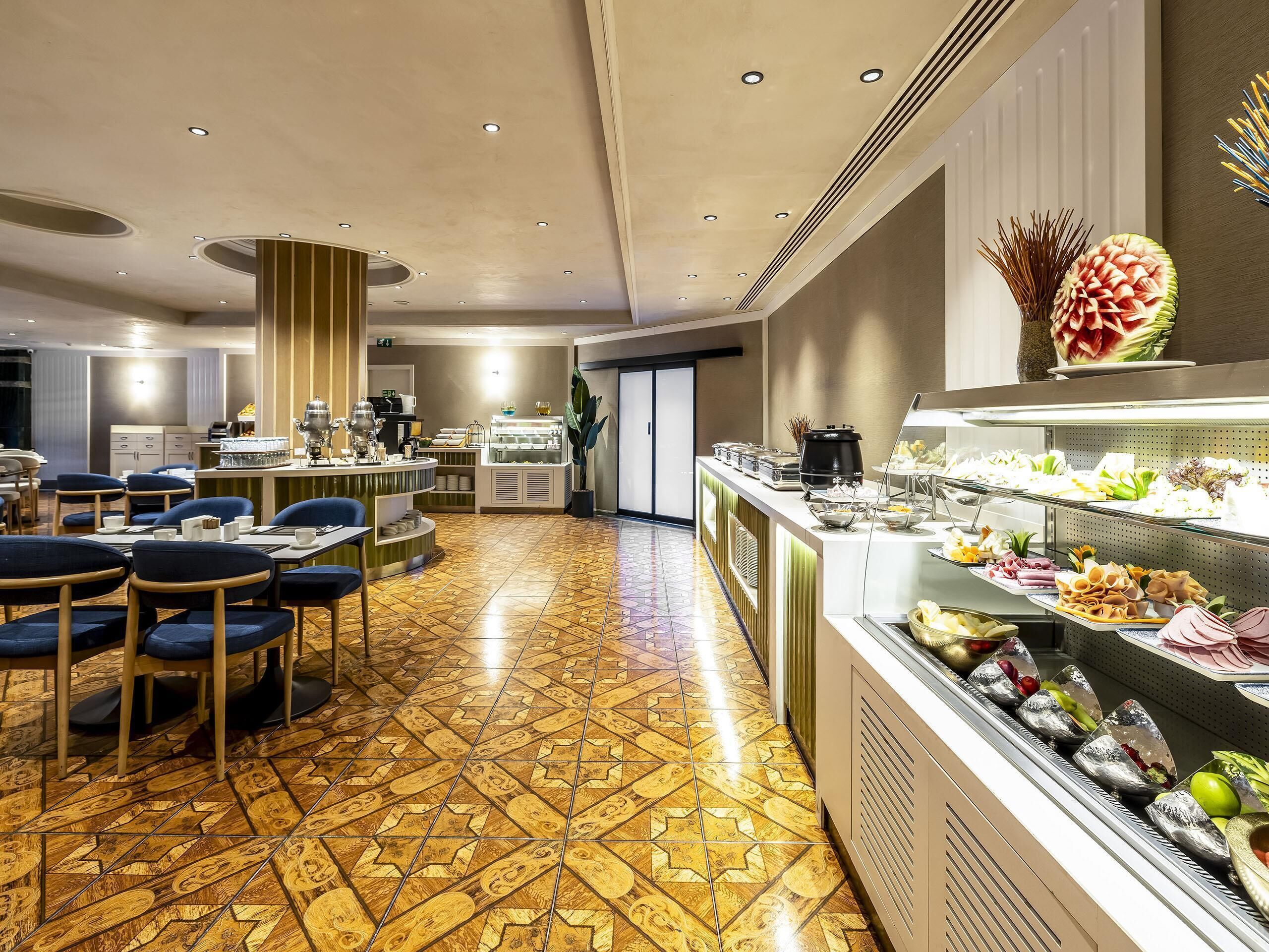 Un espace de restauration d’hôtel avec un buffet, comprenant différents stands de nourriture et différentes configurations de tables et de chaises.