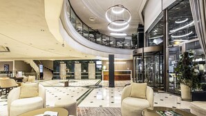 Un vestíbulo amplio con una zona de estar central, un mostrador de recepción y una escalera que lleva a un nivel superior.