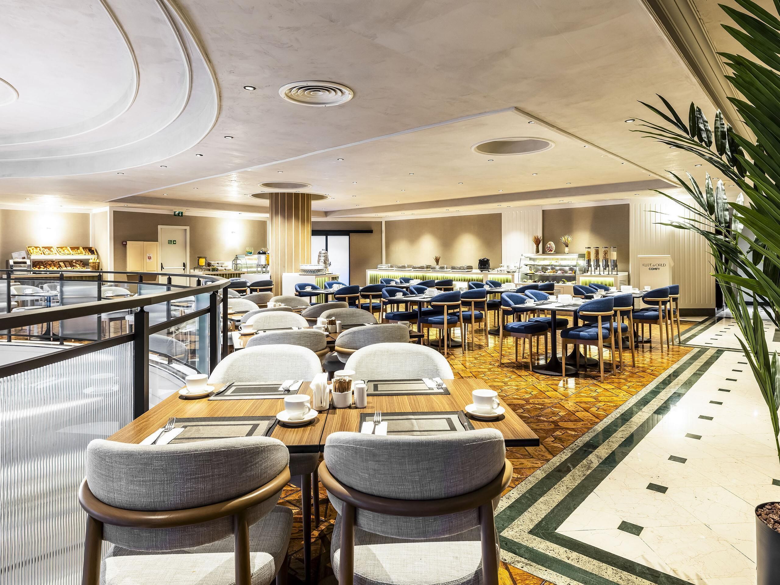 Un comedor de hotel con varias mesas y sillas, un bufé y vistas al vestíbulo.