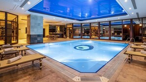 Una amplia piscina interior con techo de tragaluces, rodeada de zonas de descanso con mesas y sillas.