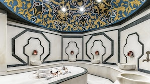 Un baño lujoso con suelo de mármol, una bañera independiente y apliques de pared ornamentados.