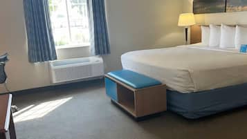 Una habitación de hotel con cama, mesita de noche, lámpara, ventana con cortinas y aire acondicionado.