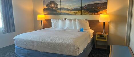 A hotel room with a large bed, two bedside lamps, a nightstand, and a view of a landscape painting.