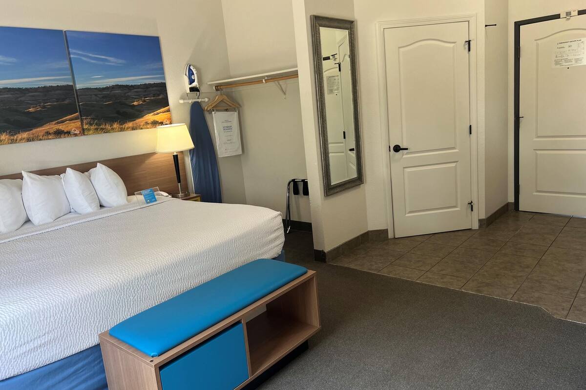 A hotel room with a large bed, a bedside table, a mirror, and a view of the landscape through the window.