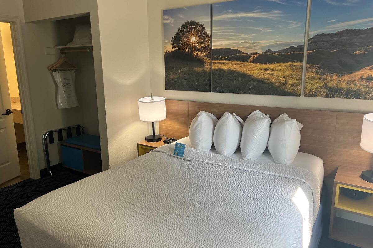 A hotel room with a large bed, a nightstand with a lamp, a desk with a chair, and a wardrobe.