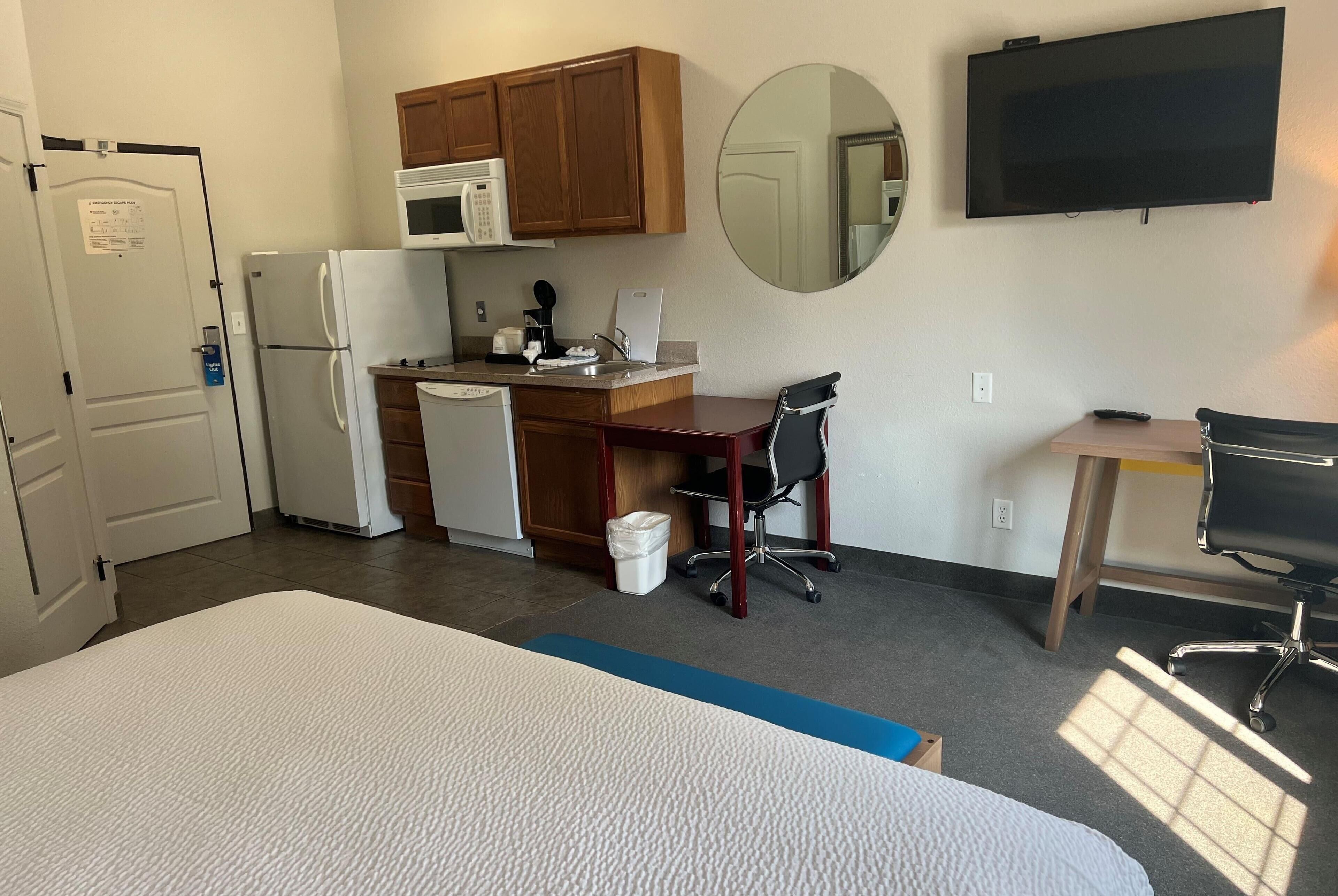 Habitación de hotel pequeña con cama, kitchenette, escritorio y televisor.