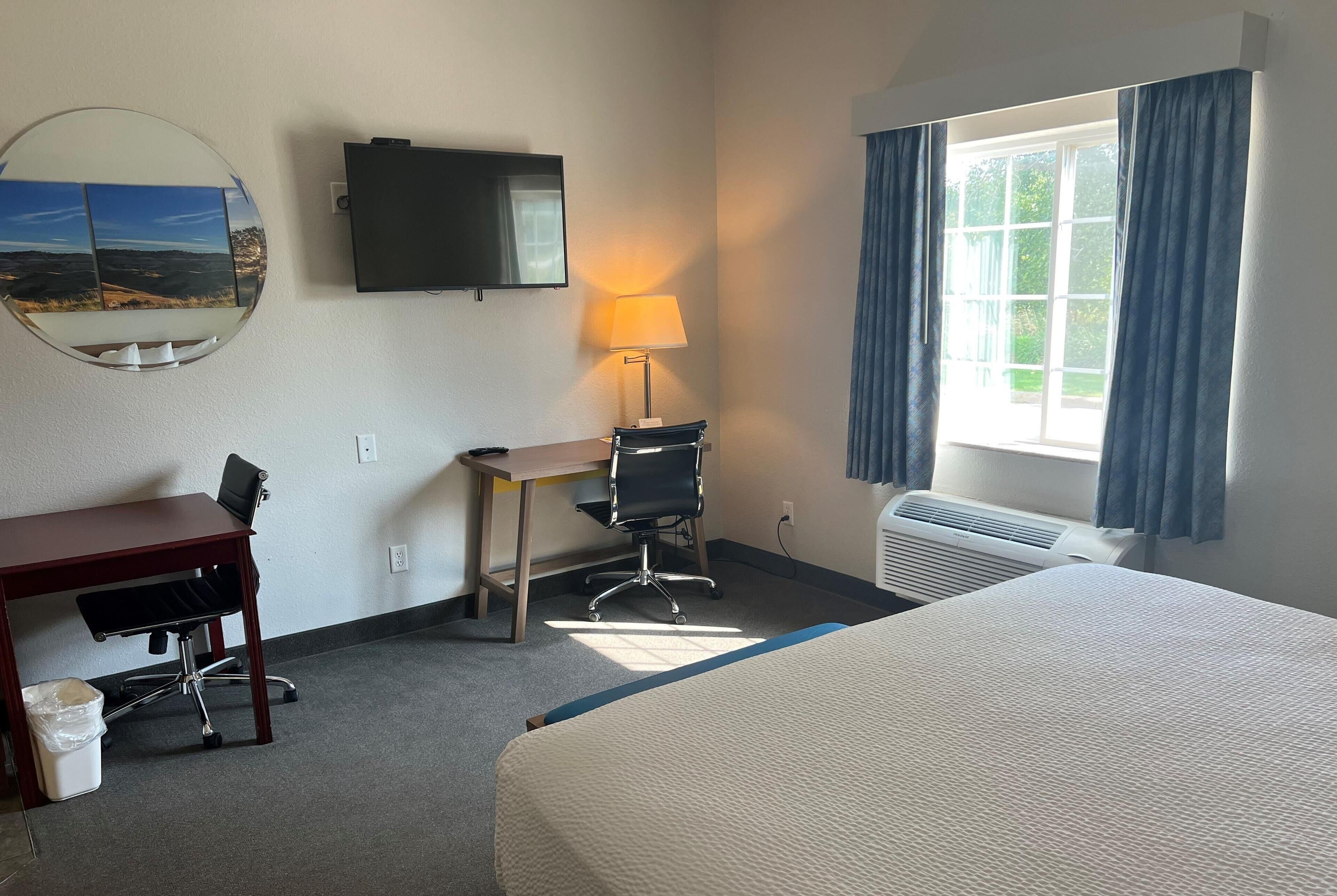 A hotel room with a bed, a desk with a chair, a television, a lamp, and a window with curtains.