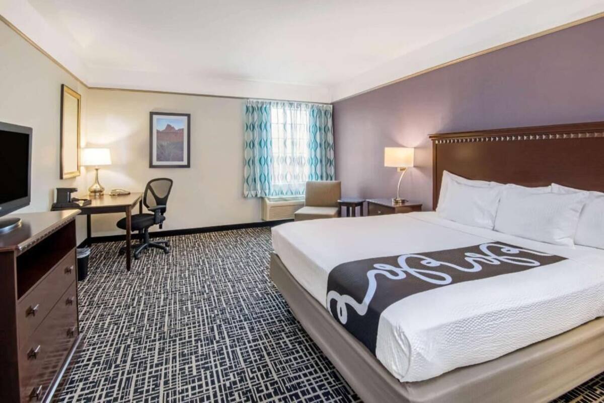 A hotel room with a bed, desk, chair, TV, and a patterned carpet.