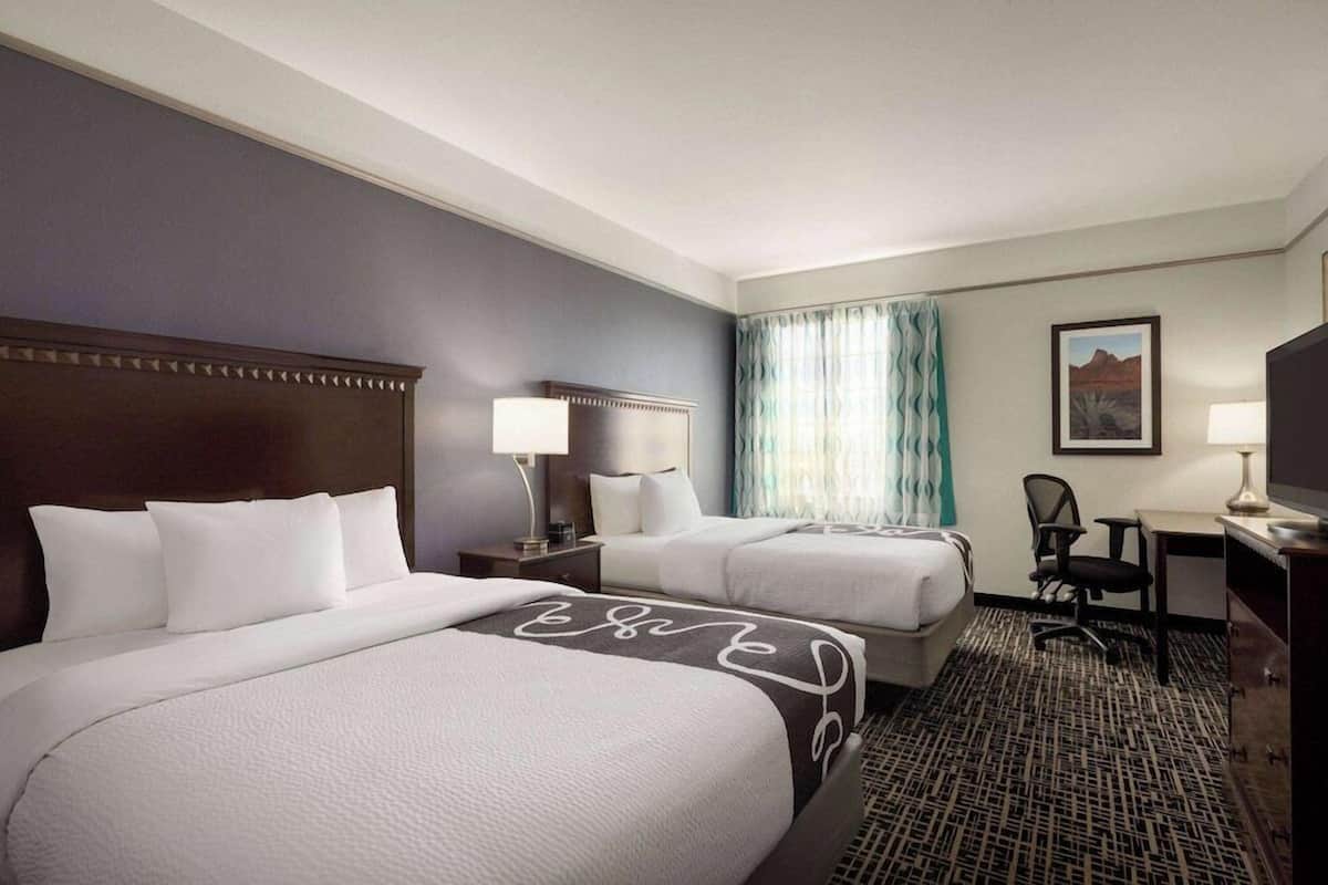 A hotel room with two beds, a desk, a chair, a TV, and a window with curtains.
