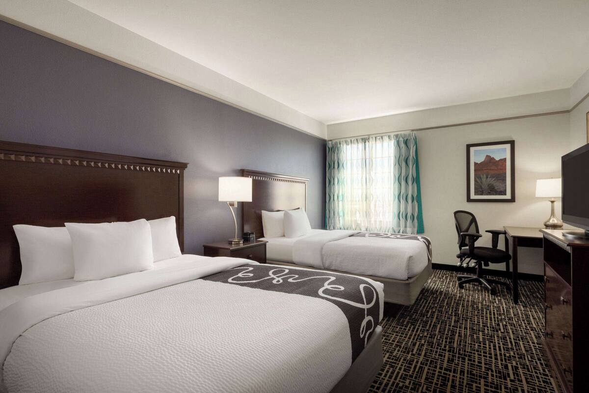 A hotel room with two beds, a desk, a chair, a television, and a window with curtains.