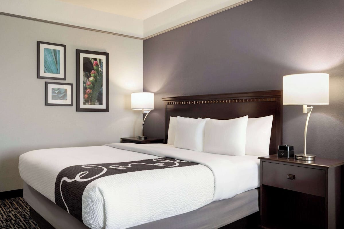 A neatly made bed with a white and dark patterned blanket, two bedside lamps, and framed pictures on the wall.
