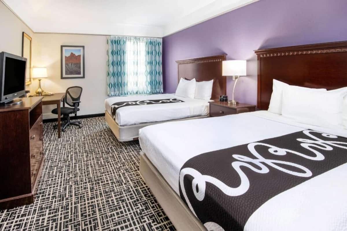 A hotel room with two beds, a desk with a television, a chair, and a patterned carpet.