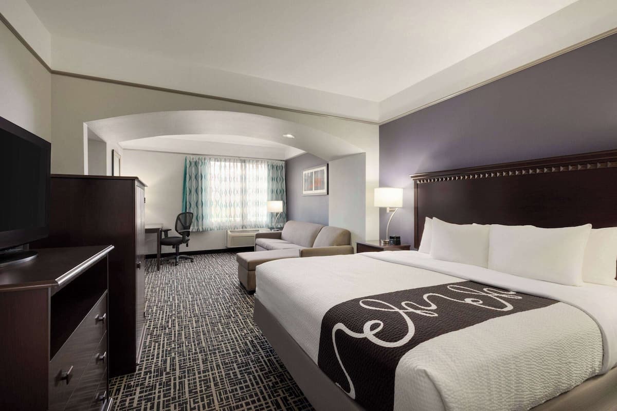 A hotel room with a large bed, a desk, a chair, a TV, and a window with curtains.