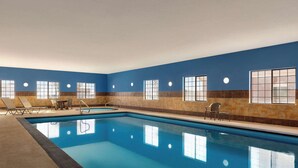 An indoor swimming pool with clear blue water, surrounded by beige and brown tiled walls, and equipped with sun loungers and a small table. - La Quinta Inn & Suites by Wyndham Dumas (Dumas)