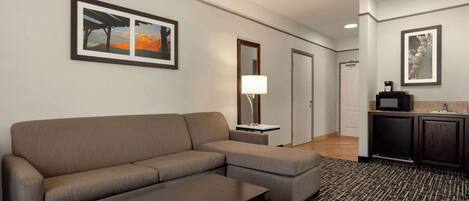 Una habitación de hotel moderna con un sofá modular, una mesita, un tapete estampado, un televisor y una zona de kitchenette.