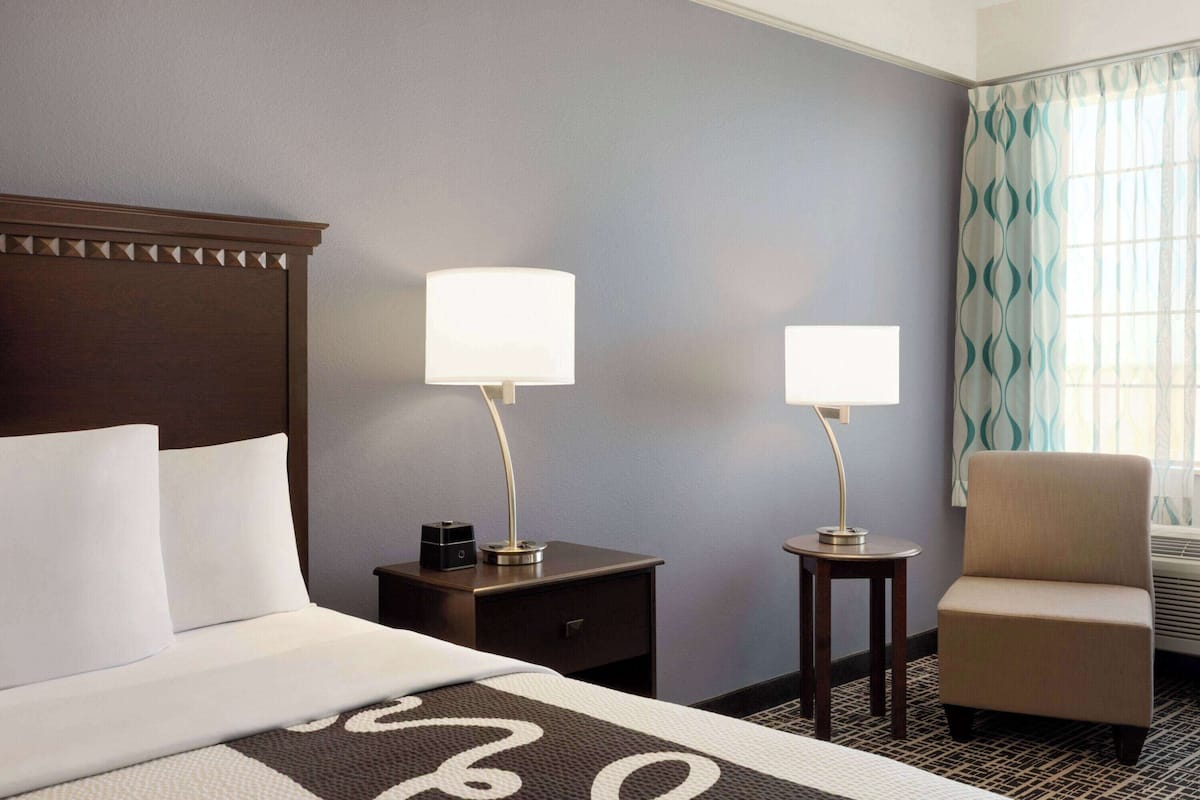 A hotel room with a bed, two bedside lamps, a chair, and a window with curtains.