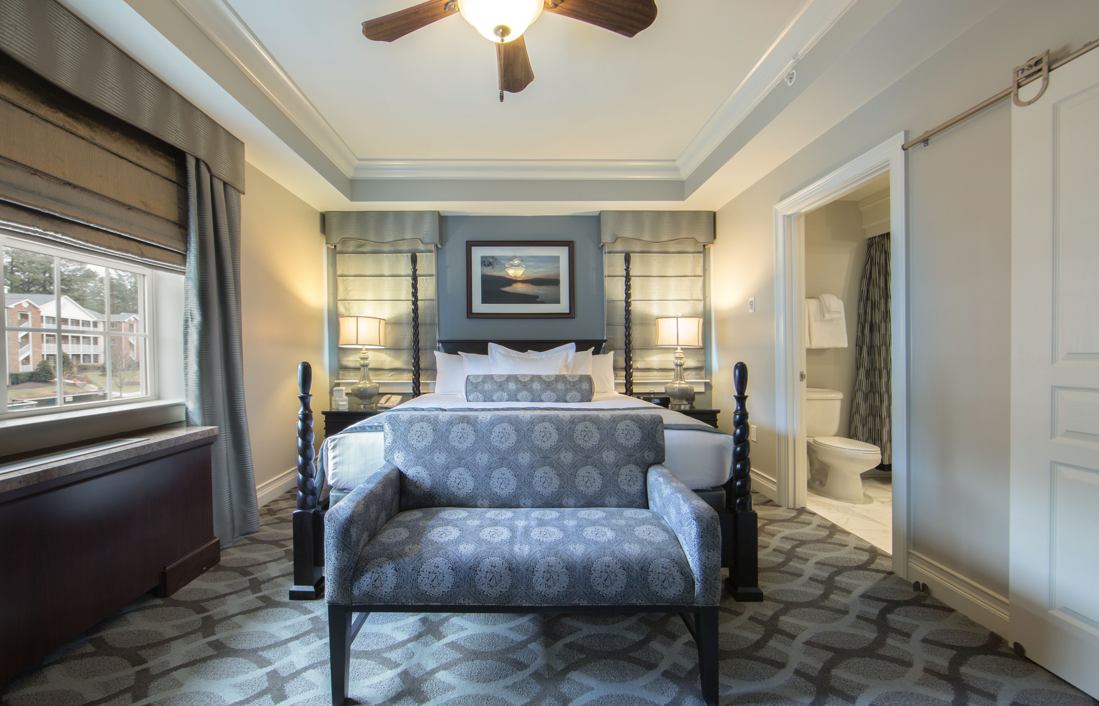 A bedroom with a bed, bedside lamps, a window, a radiator, and a ceiling fan.