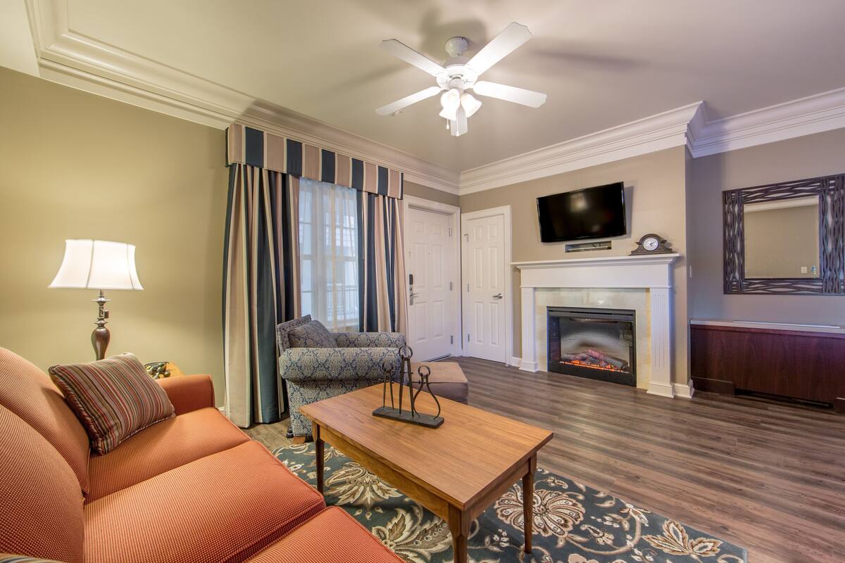 A living room with a sofa, a coffee table, a fireplace, a television, and a ceiling fan.