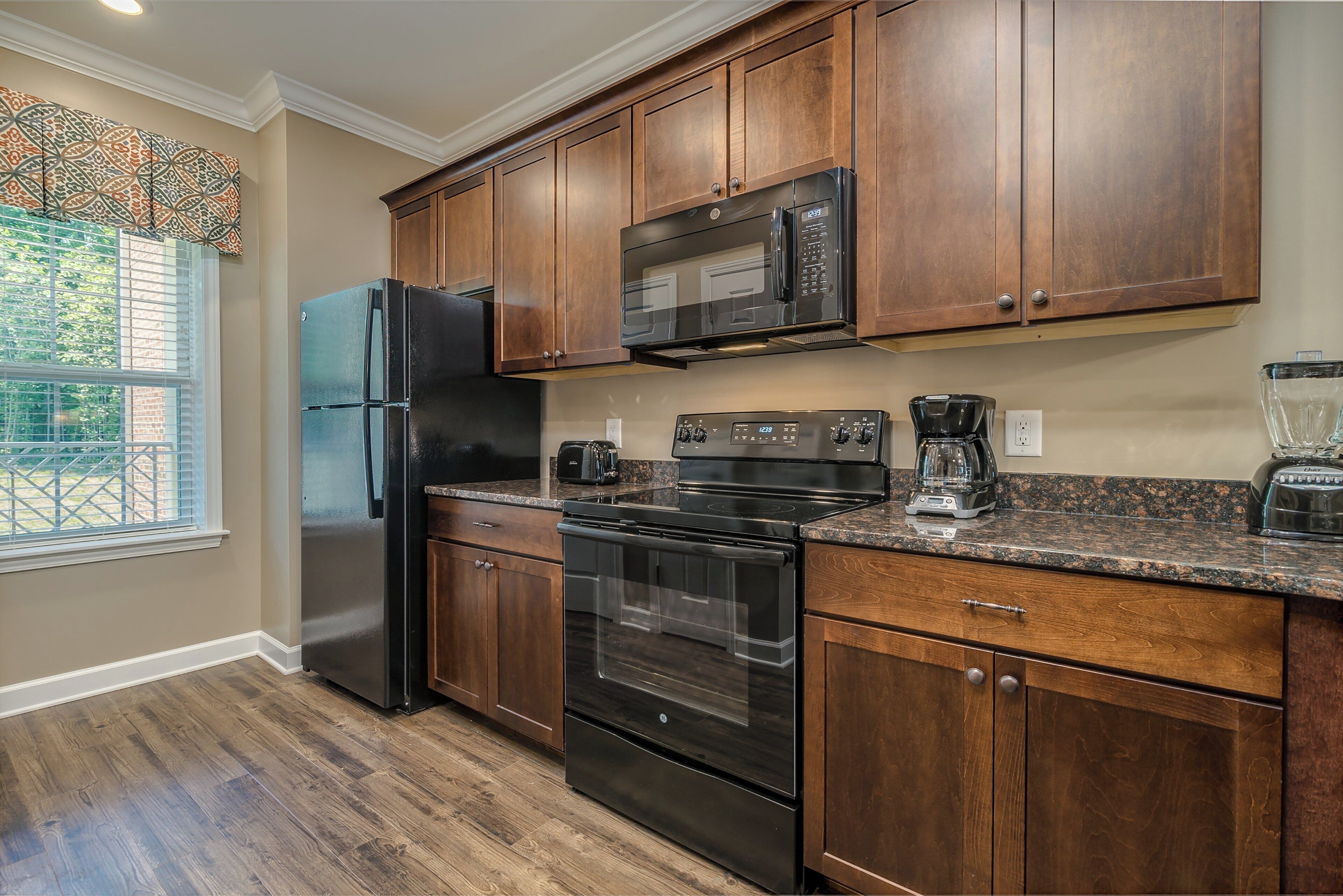 A kitchen with wooden cabinets, a refrigerator, a microwave, a stove, and a coffee maker.