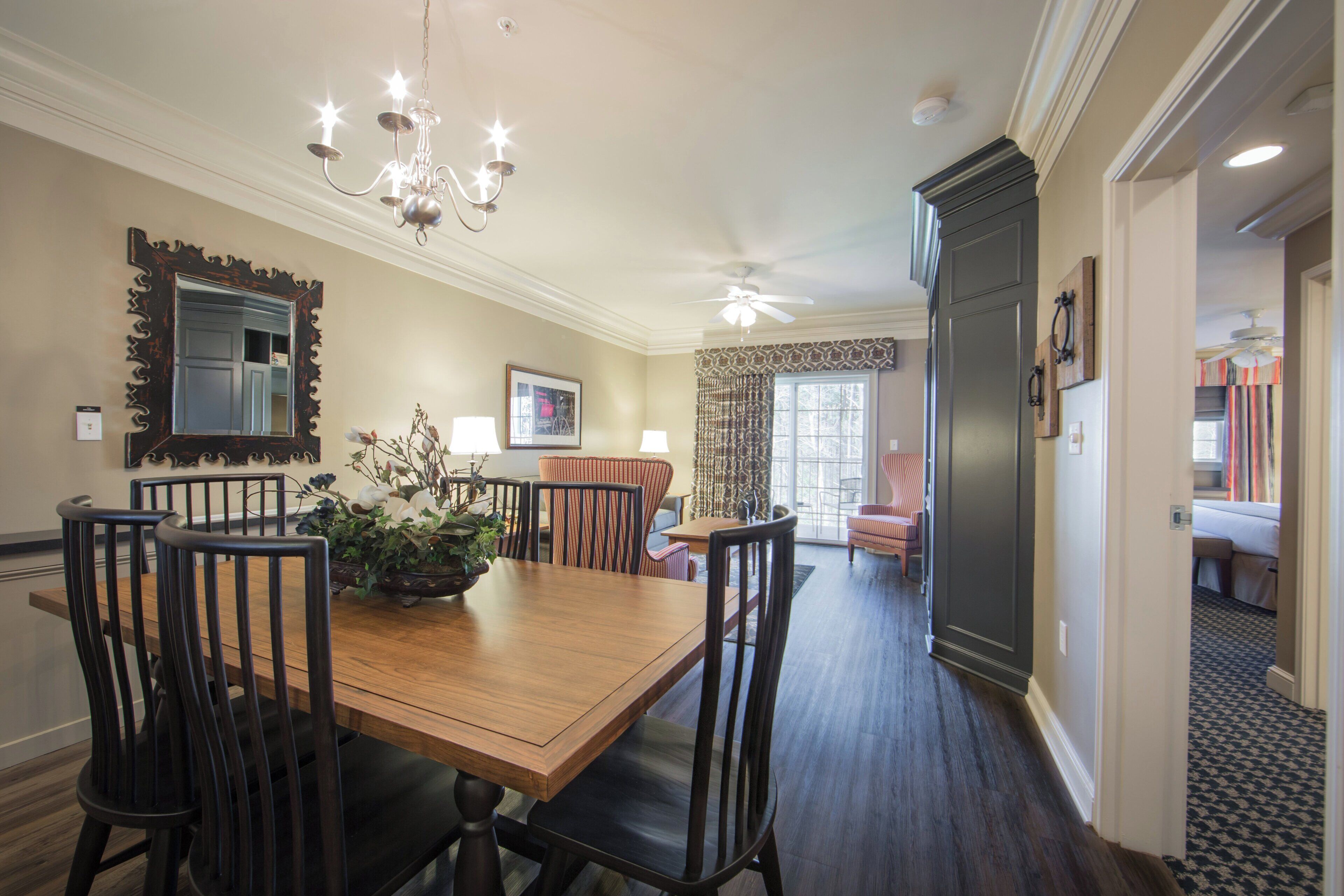 A dining area with a wooden table, chairs, a chandelier, and a mirror on the wall.