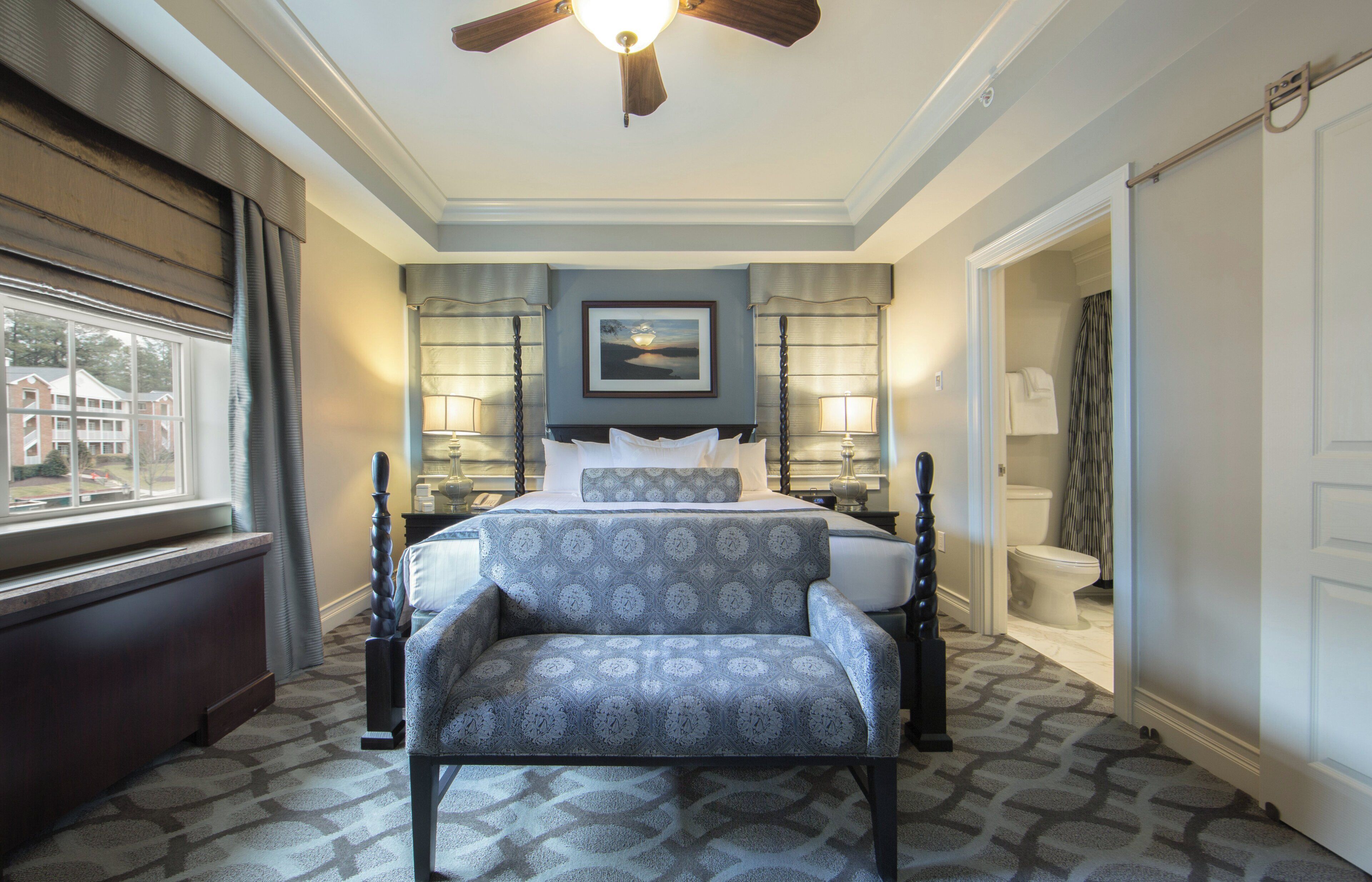 A hotel room with a bed, a chair, a desk, a window, and a bathroom.