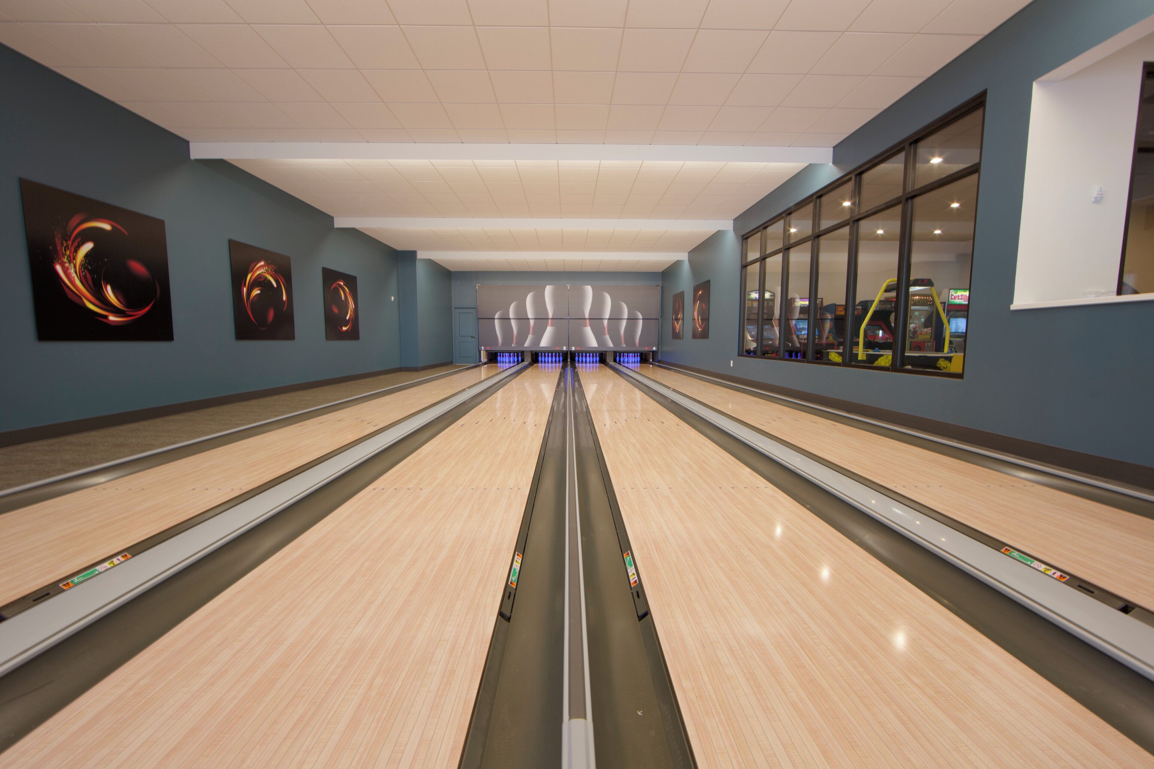 A bowling alley with multiple lanes, a ceiling with recessed lighting, and wall art.