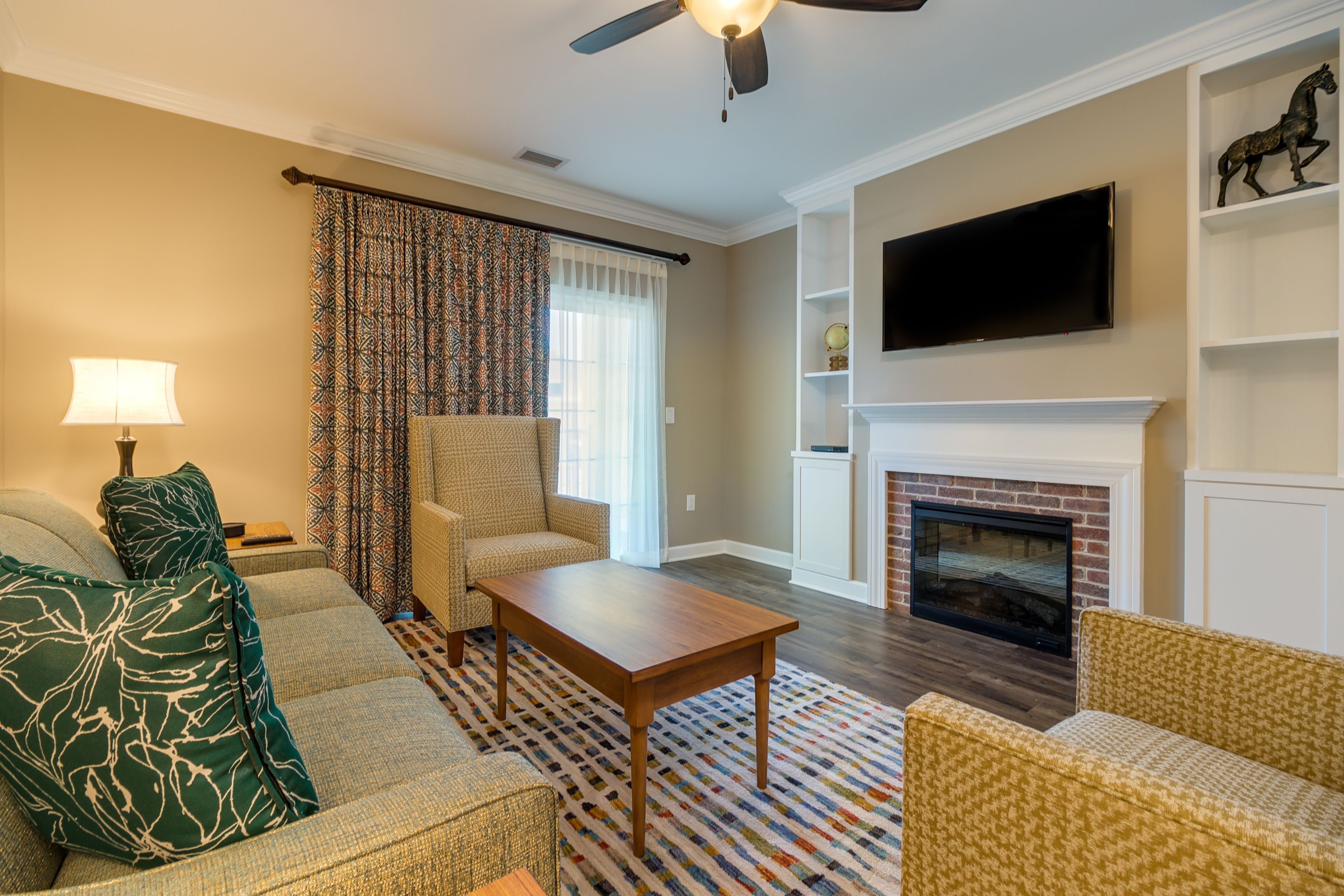 A living room with a sofa, armchair, coffee table, fireplace, television, and patterned curtains.