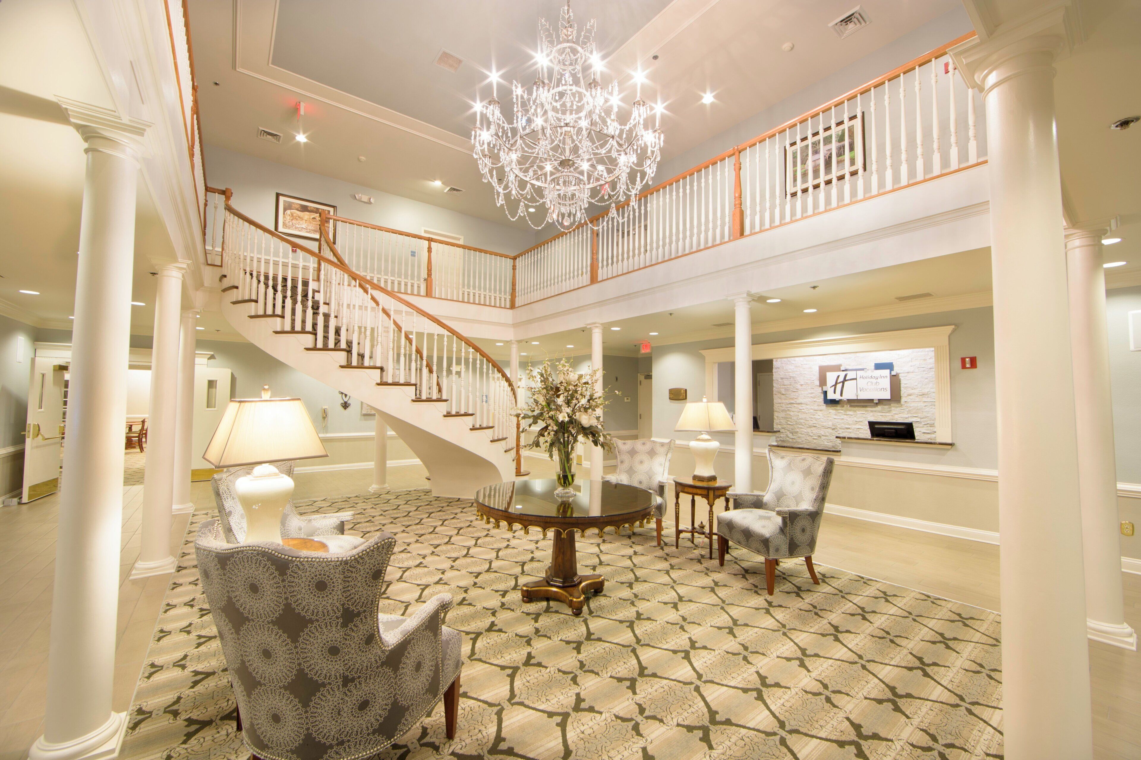 A spacious lobby with a grand staircase, a chandelier, and a reception desk.