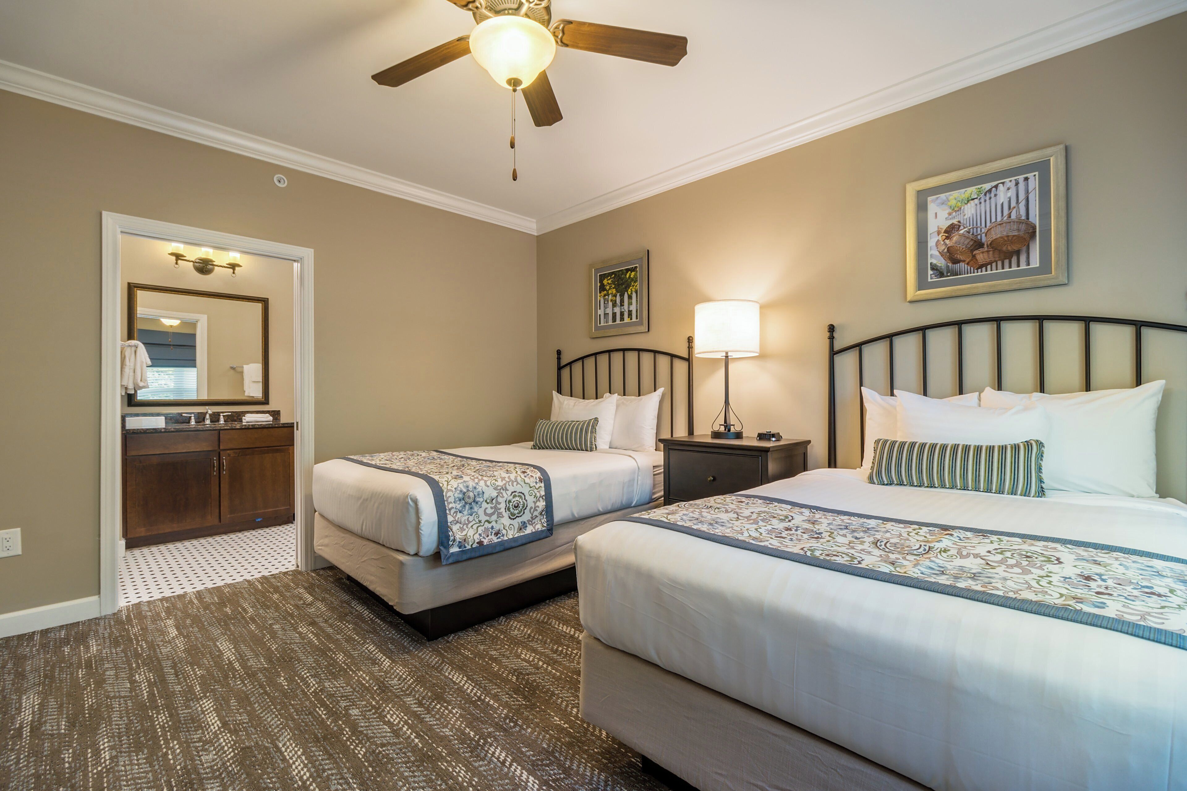 A hotel room with two beds, a bathroom, and a ceiling fan.