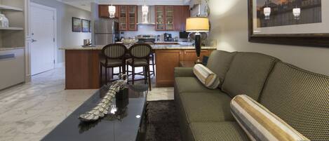 A modern kitchen with a central island, dining chairs, a sofa with a decorative pillow, and a framed picture on the wall.