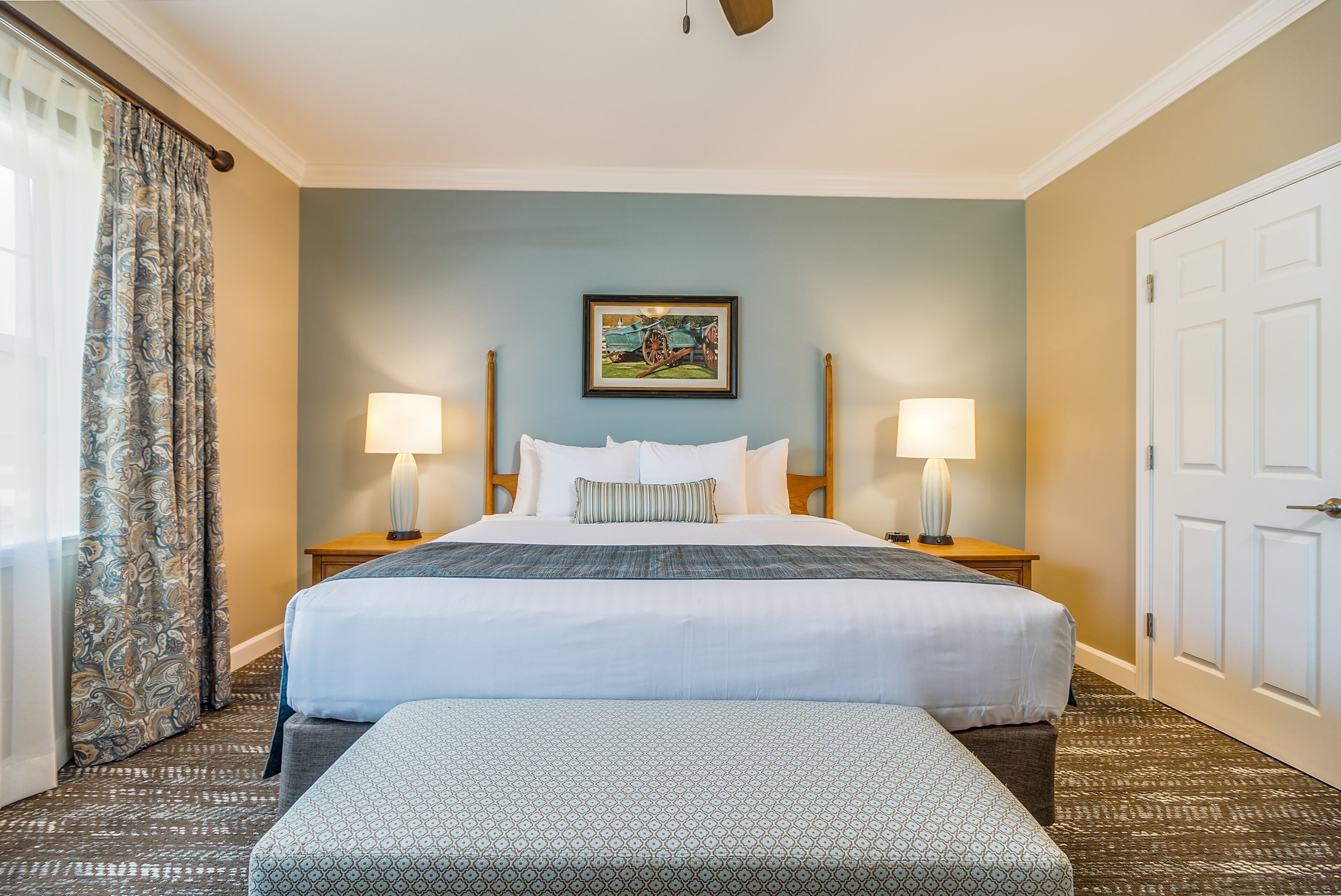 A hotel room with a large bed, two bedside tables with lamps, a painting on the wall, and a patterned carpet.