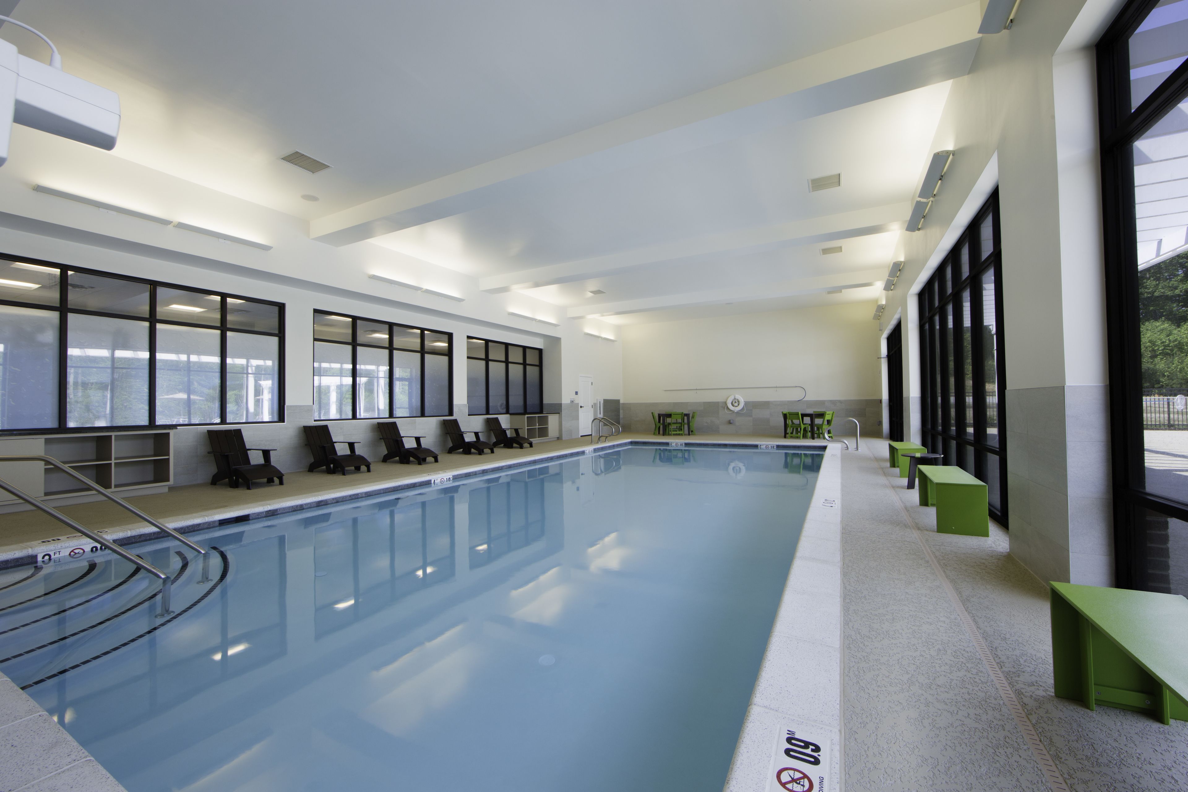 Une piscine intérieure moderne avec des parois en verre transparent, des bancs verts et un sol carrelé.