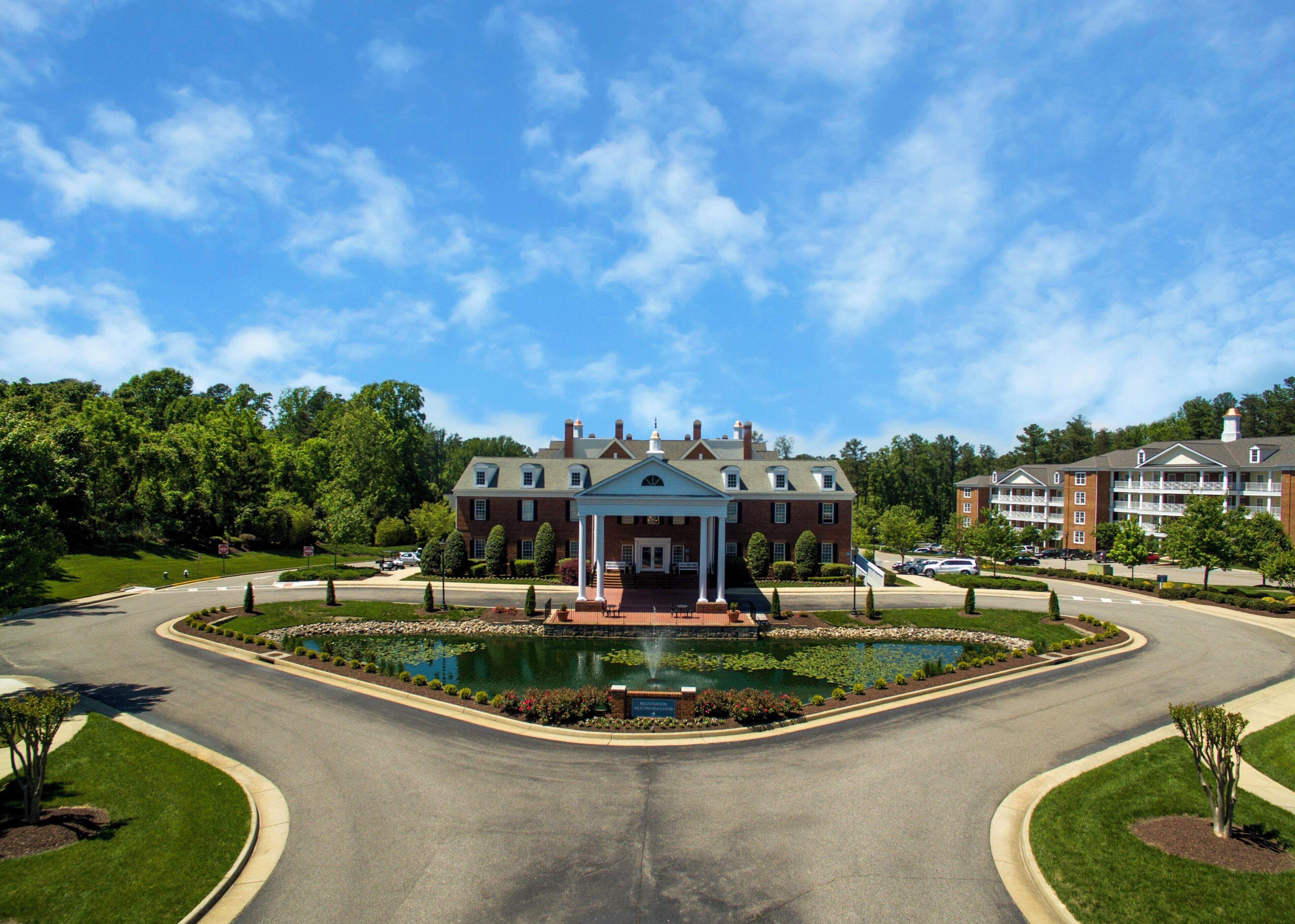 A large brick building with a central pavilion, a landscaped pond, and a well-maintained lawn.