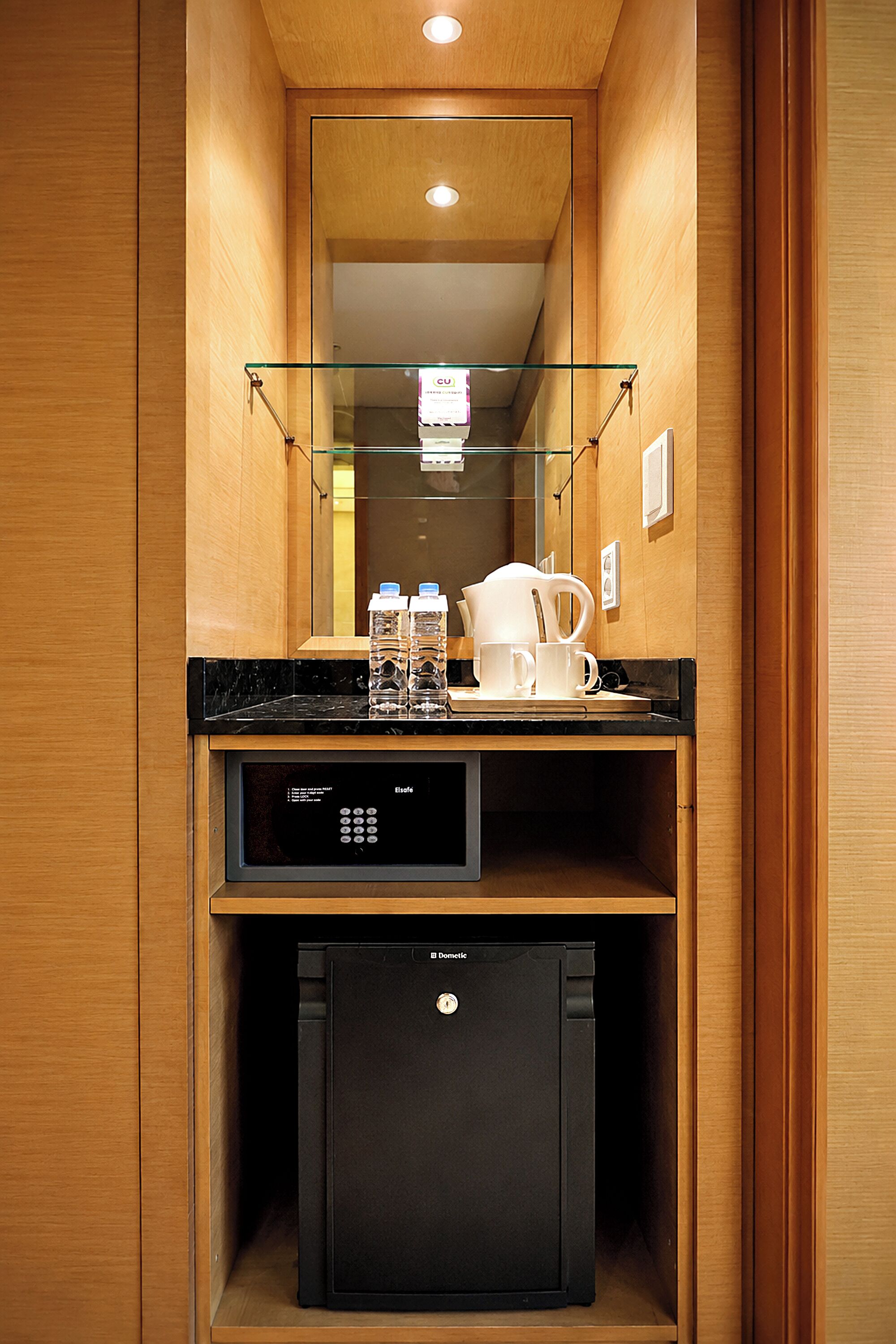 Una kitchenette compacta con cafetera, botellas de agua y un refrigerador pequeño.