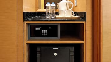 Una kitchenette compacta con cafetera, botellas de agua y un refrigerador pequeño.