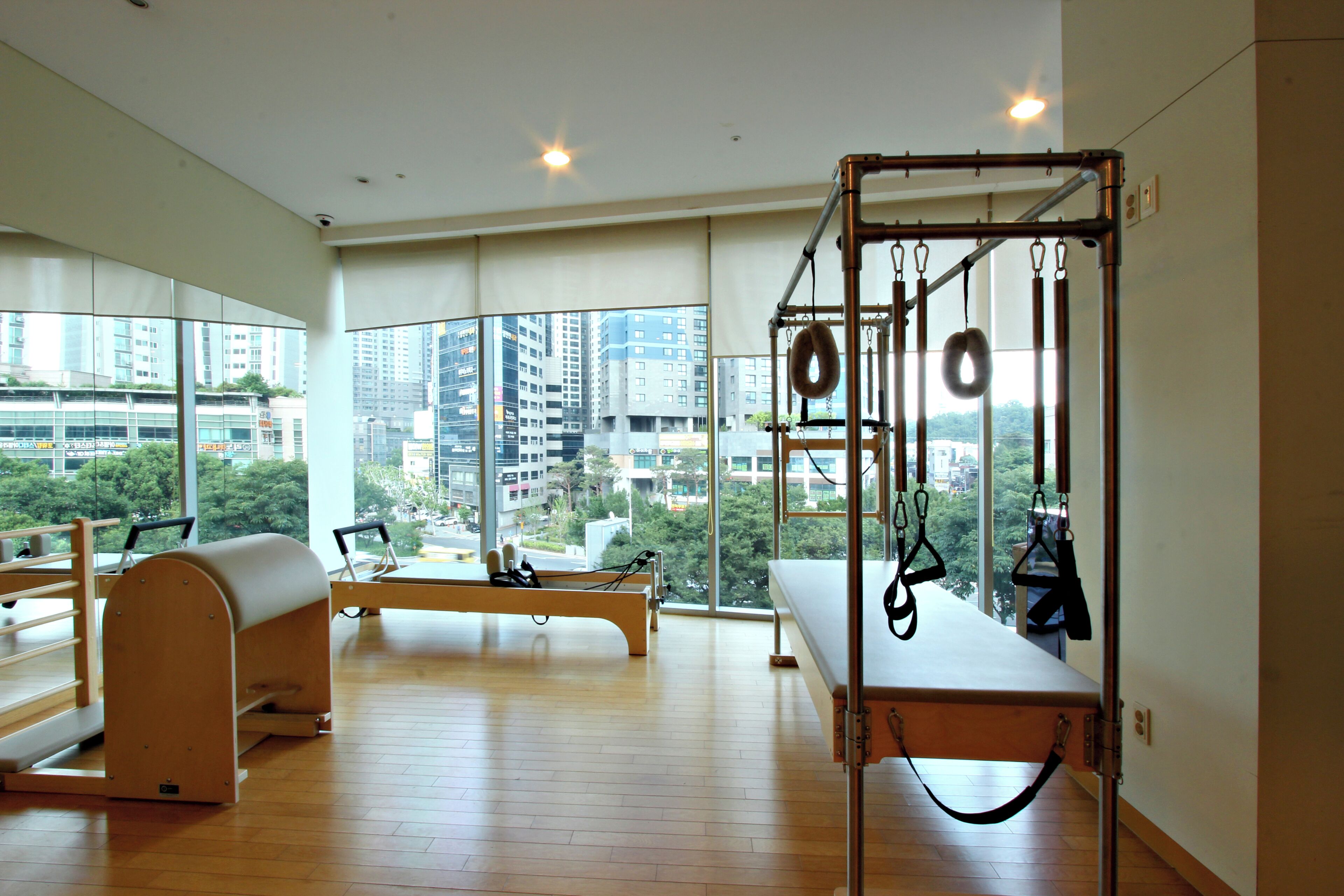 A spacious room with a Pilates reformer, a bench, and a window with a city view.