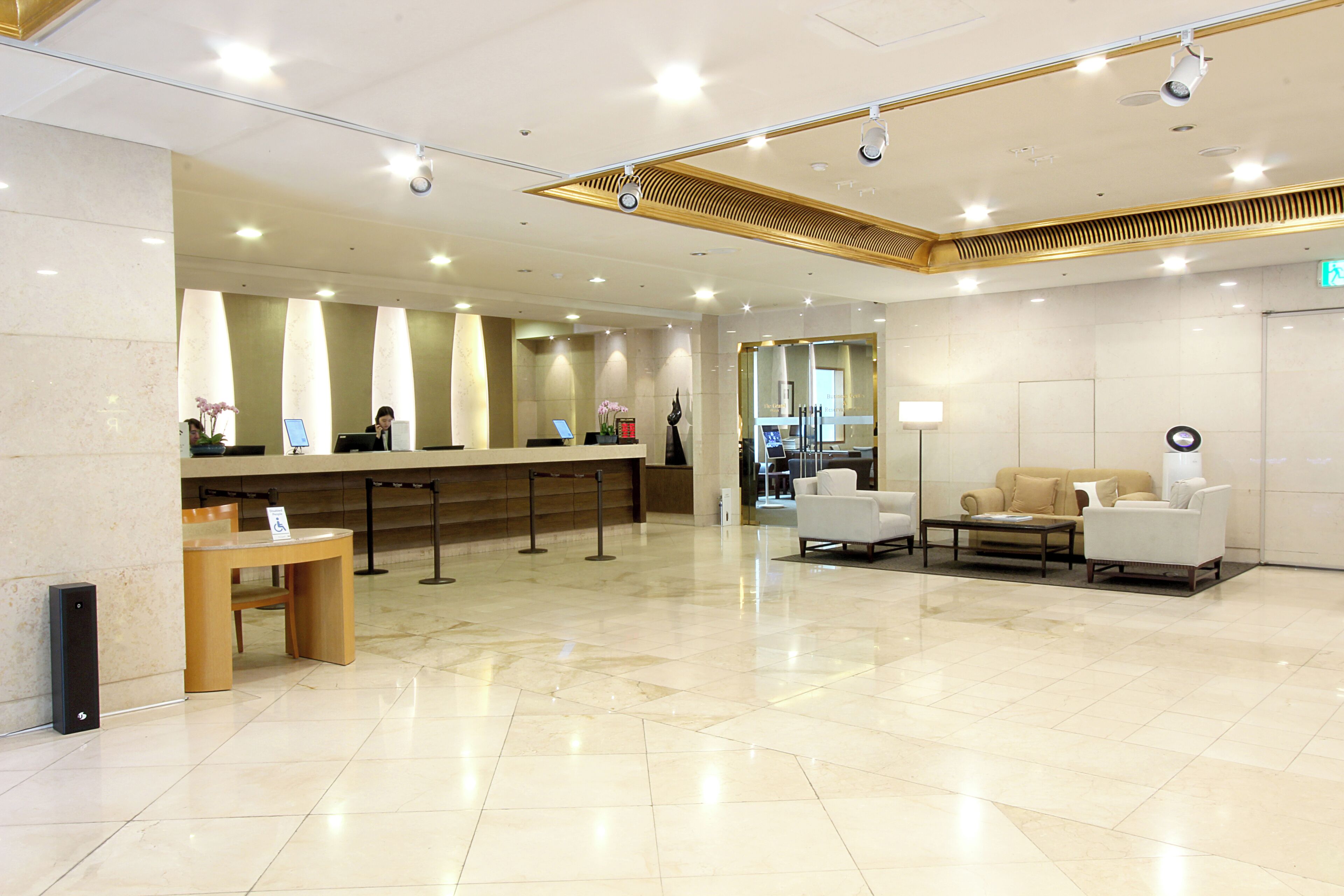 A hotel reception area with a counter, seating, and a modern ceiling design.