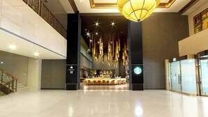 A spacious lobby with a central bar area, a staircase on the left, and a large chandelier. - Grand Hotel (Daegu)
