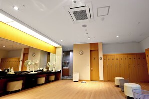A hotel room with a wooden floor, a mirror, a desk with a chair, a scale, and a wardrobe with multiple compartments.