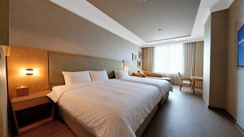 A hotel room with two beds, a desk, a chair, and a large window with curtains.