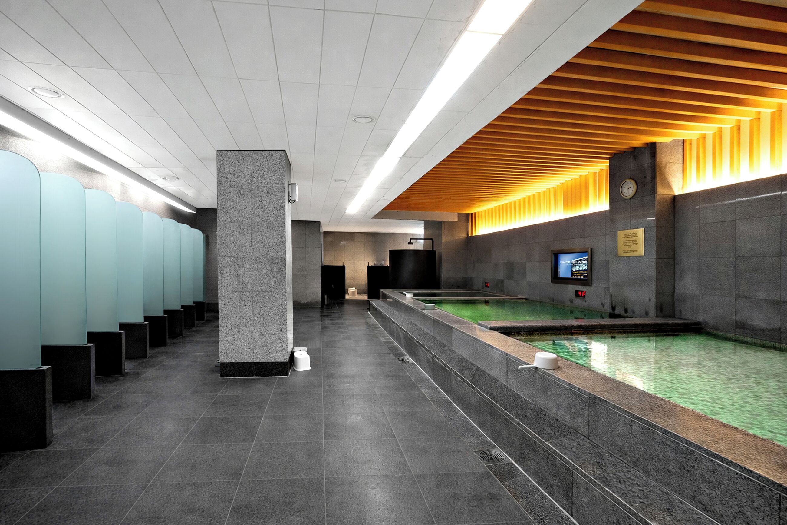 A modern bathroom with a long row of sinks, a large pillar, and a pool area.