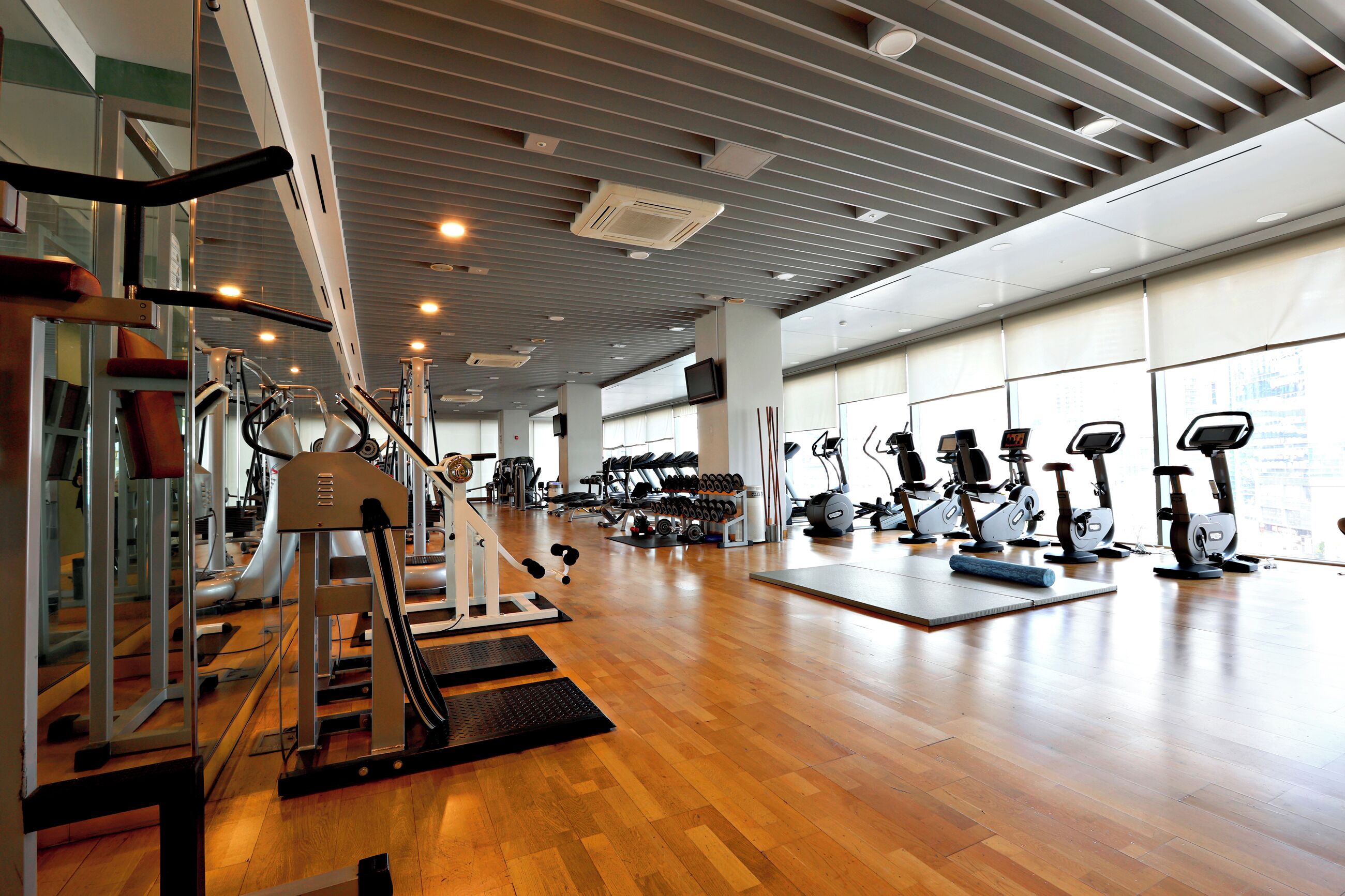 A gym with various exercise equipment, wooden flooring, and large windows.