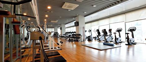 A gym with various exercise equipment, wooden flooring, and large windows.