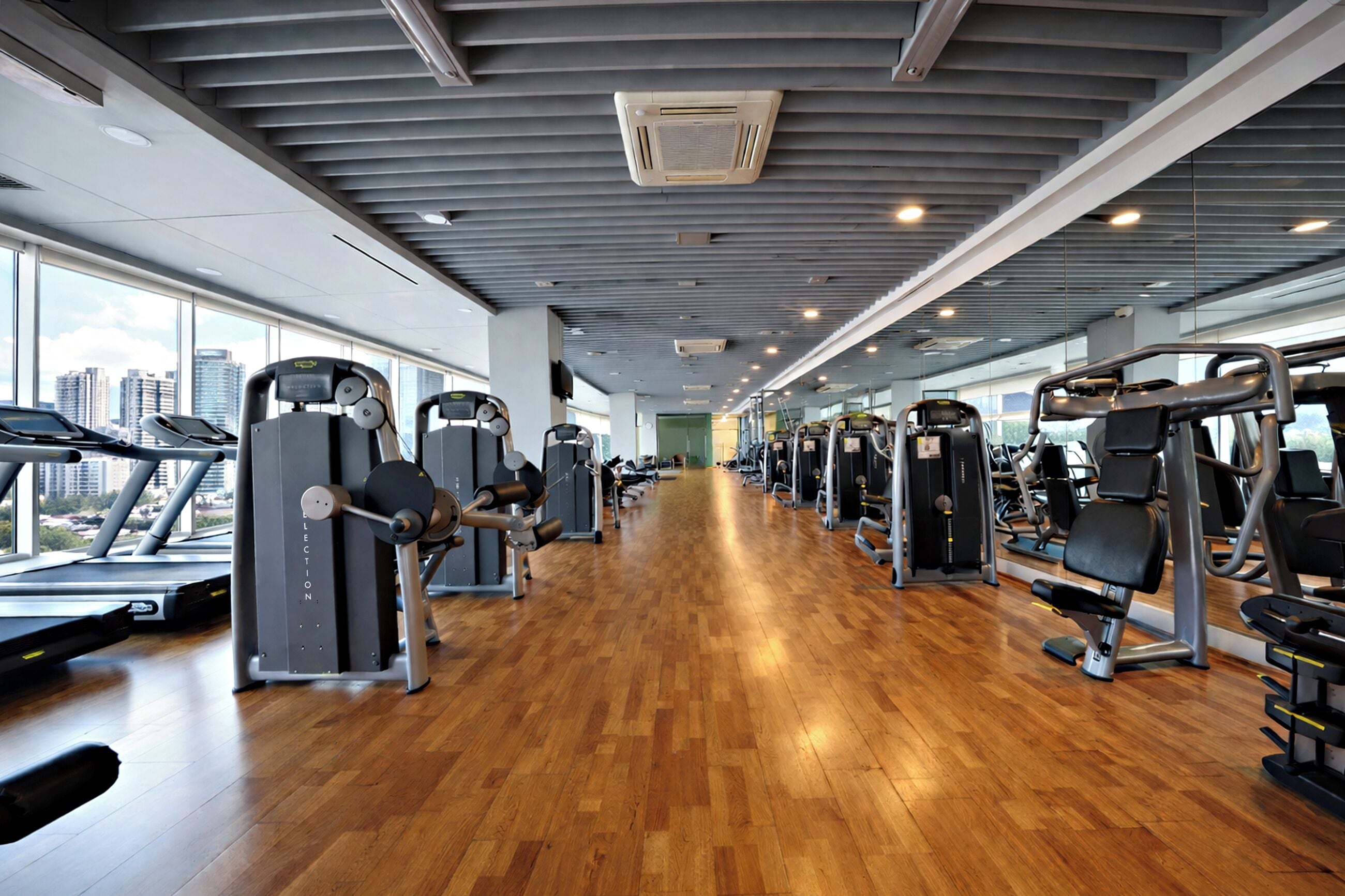 Un gimnasio con cintas de correr, máquinas de pesas y suelo de madera.