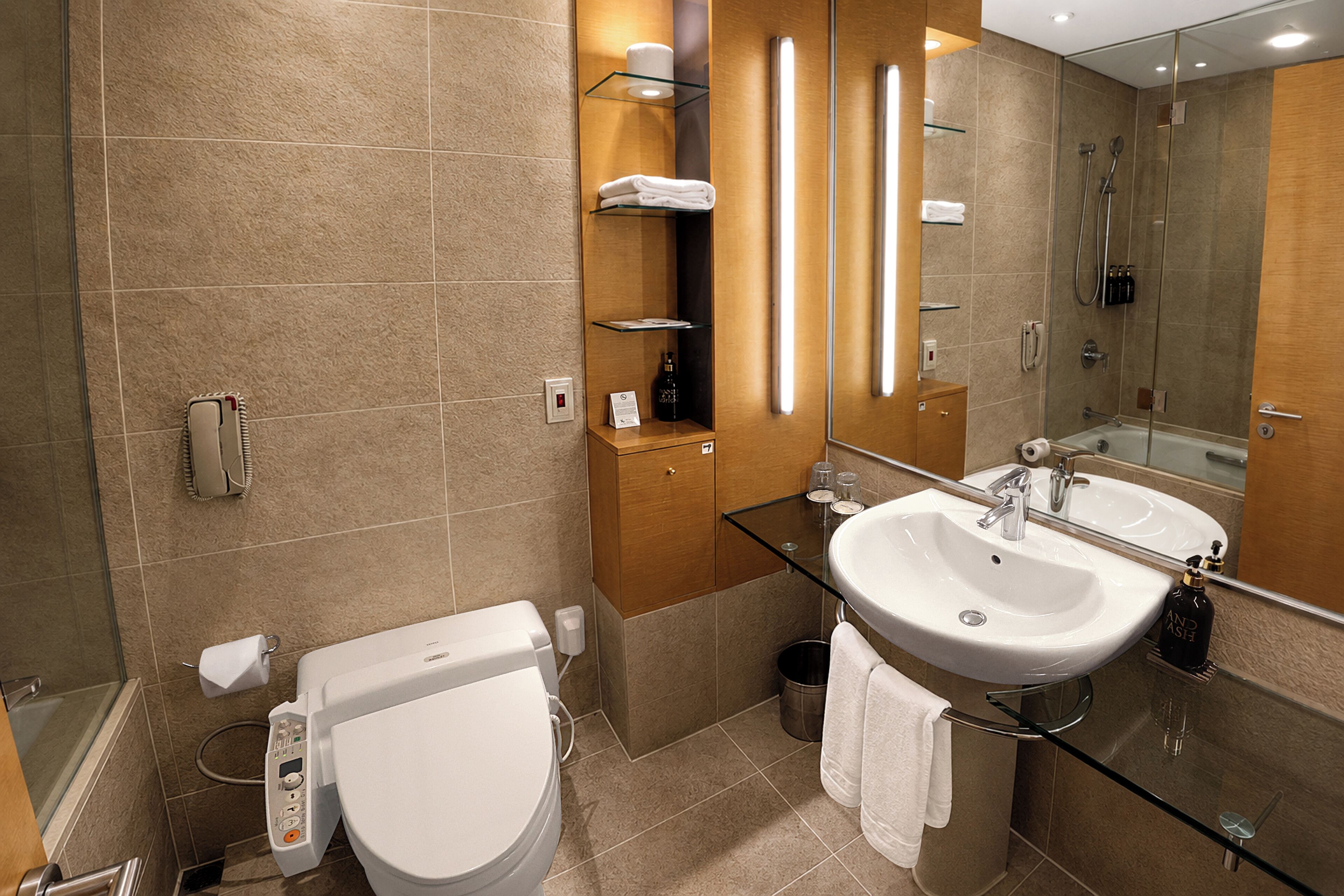 A modern bathroom with a glass-enclosed sink, a toilet, and a shower area.