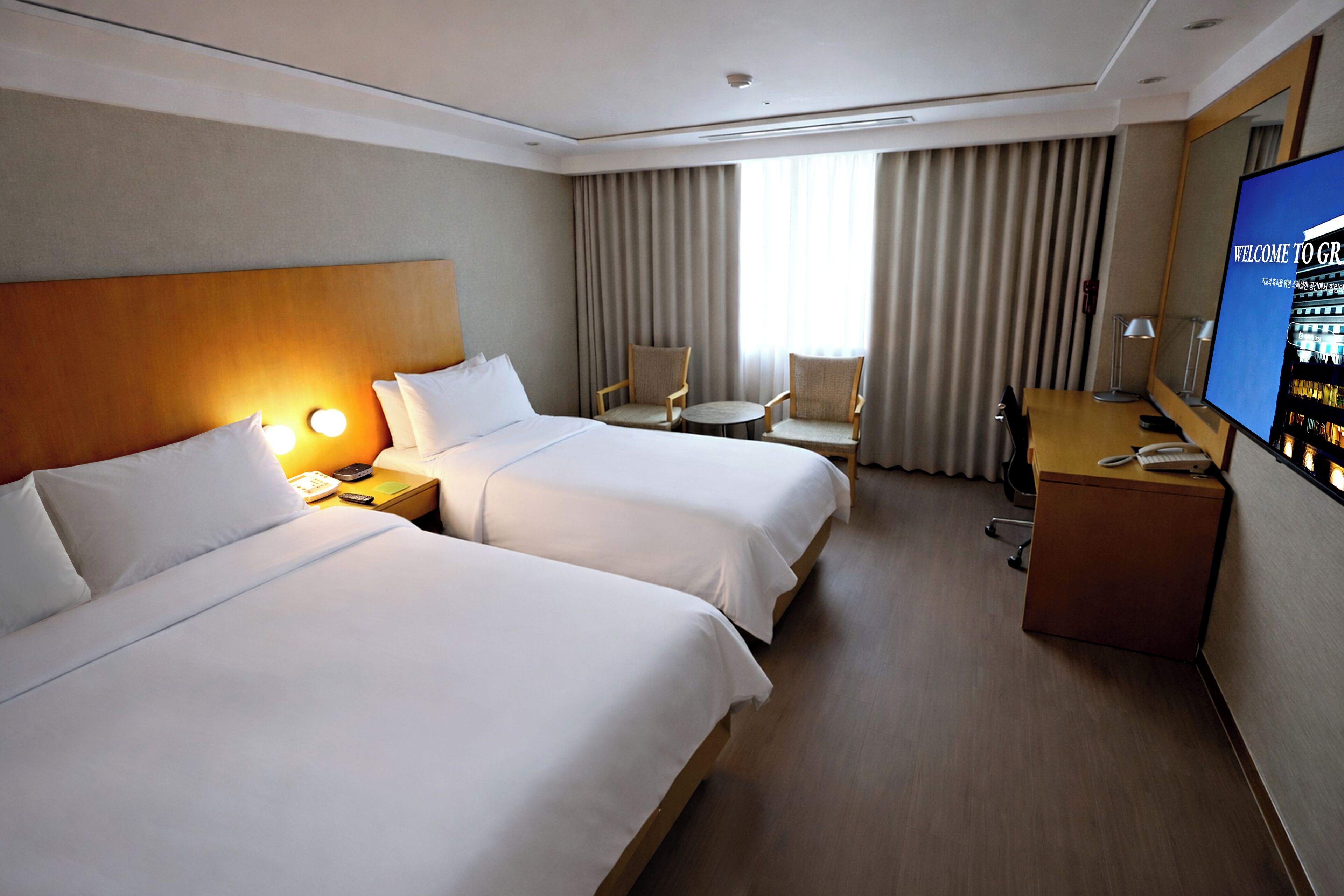 A hotel room with two beds, a desk, a TV, and a chair.