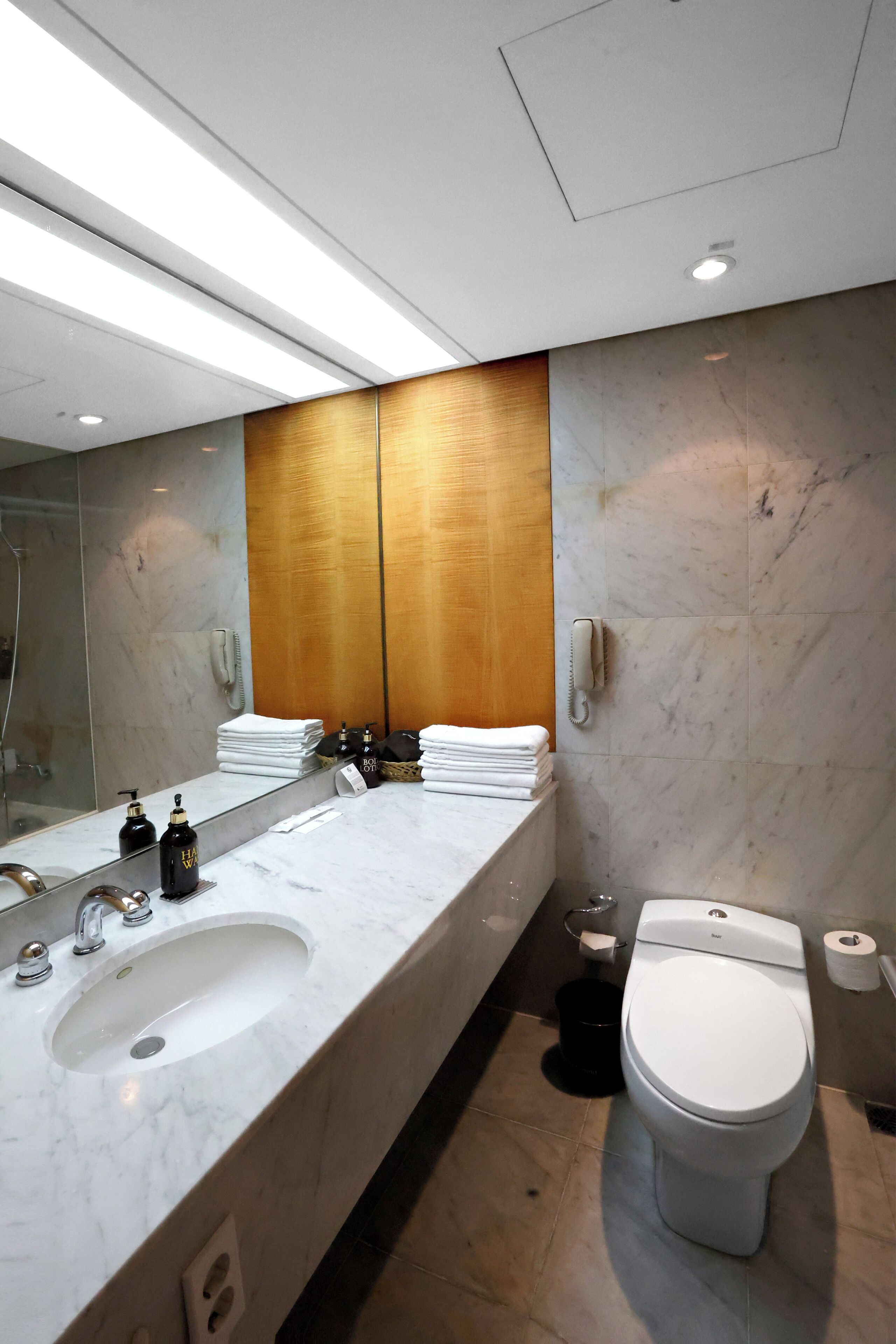 A modern bathroom with a marble sink, a white toilet, and a large mirror.